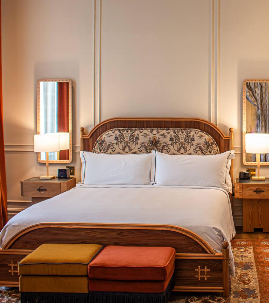 Carved wood bed with upholstered headboard and velvet benches in The Driskill Hotel